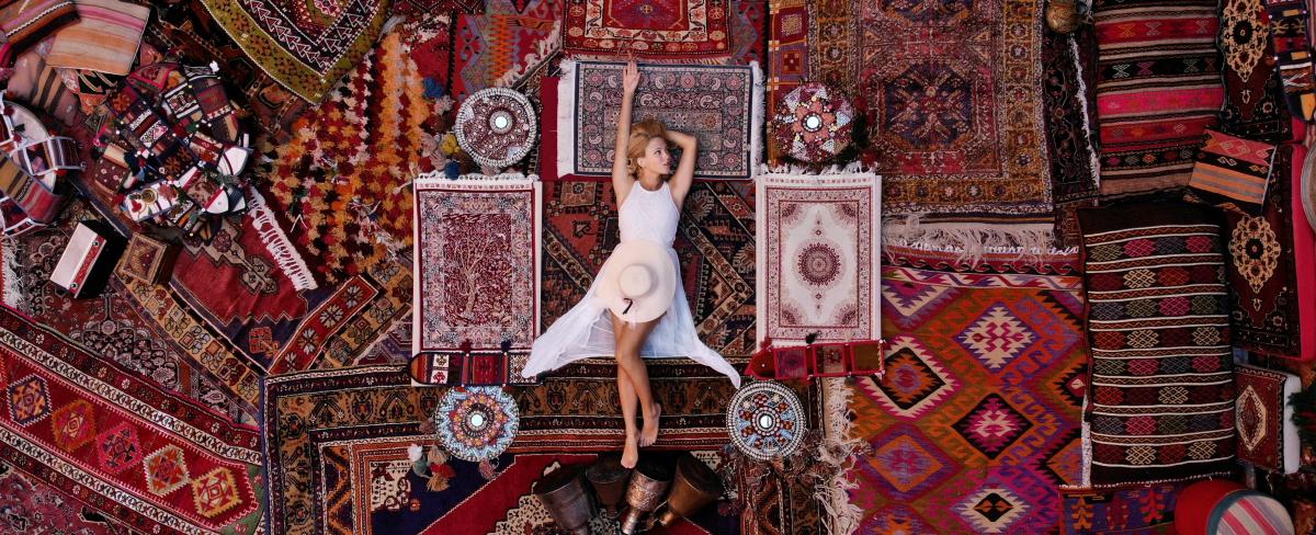 Kvind i hvid kjole ligger på orientalske tæpper med filigranmønstre.