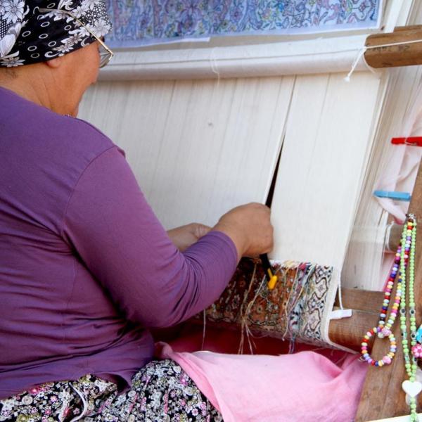Woman weaving a handcrafted Oriental carpet on a traditional loom.