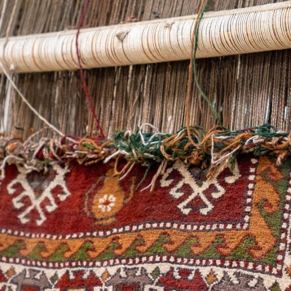 Detalje af et håndvævet tæppe ved væven med synlige kædetråde og traditionelle mønstre.