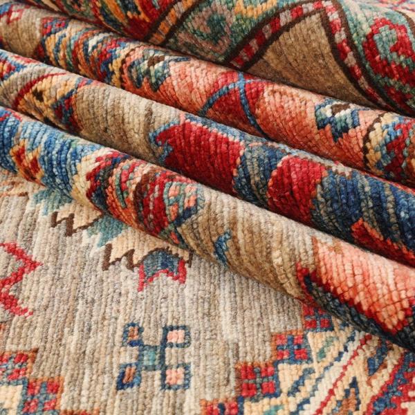 Stak af foldede kasakhanske tæpper med typisk kaukasisk mønstring i varme nuancer.