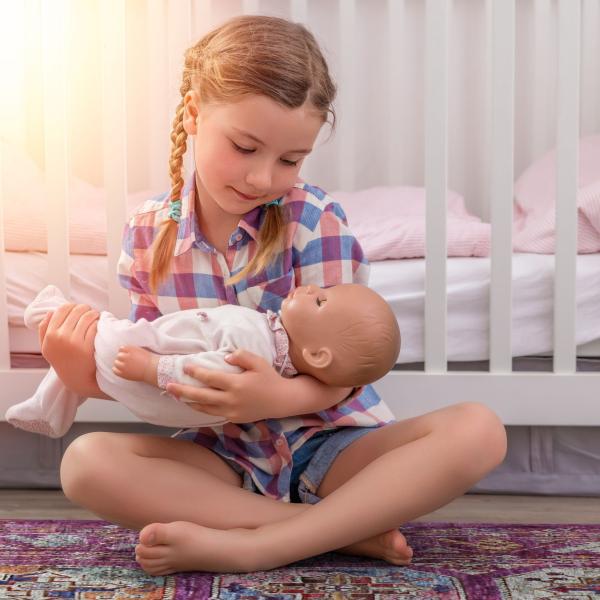 Pige med dukke i hænderne sidder på et håndknyttet orientalsk tæppe.