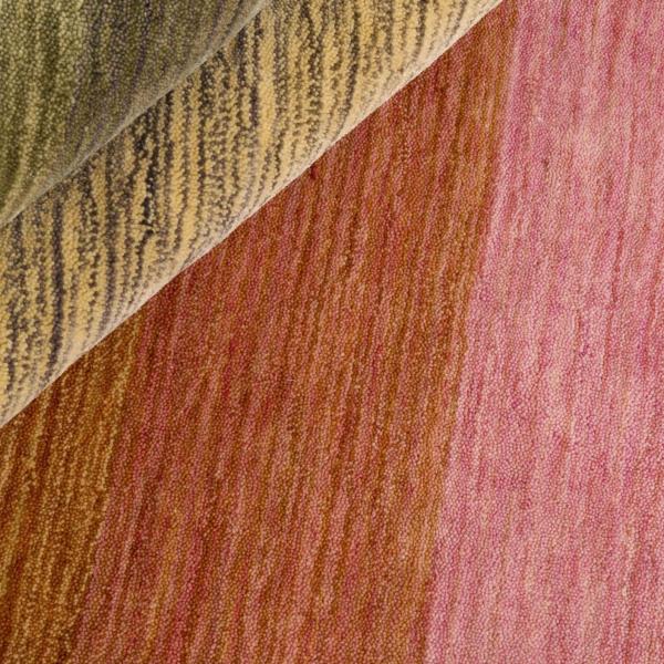 Nærbillede af overfladen på et håndknyttet tæppe i rosa- og jordfarver.