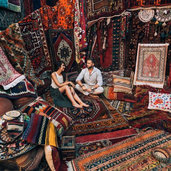 Mand og kvinde sidder på et orientalsk tæppe, omgivet af en række orientalske tæpper.