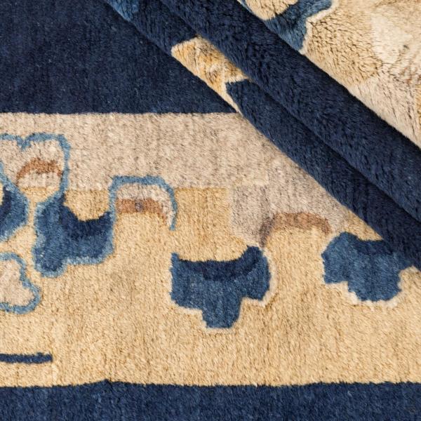 Detaljeoptagelse af en kinesisk Peking antik tæppe med floral ornamentik i beige og blå på mørk.