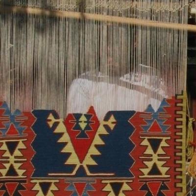 Vævning af et farverigt geometrisk kelimteppe i rød, blå og gul på væven.