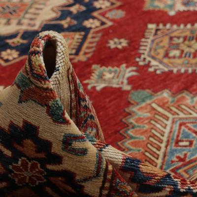 Nærbillede af et håndknyttet orientalsk tæppe med traditionelt mønster i rød, blå og creme.