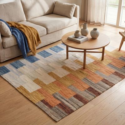 Woman sitting on a grey-blue kilim rug with a geometric pattern.