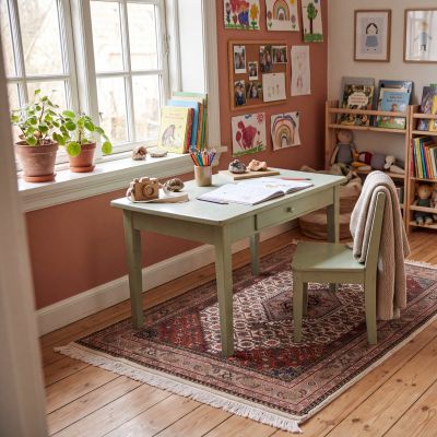 Child’s bedroom with a desk and a traditionally patterned rug in warm red and beige tones.