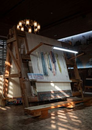 A rug loom with an unfinished carpet, where the partially woven threads are visible s
